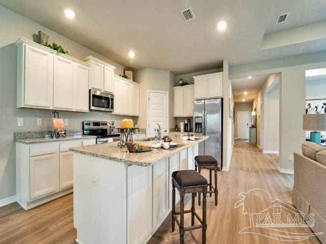 kitchen featuring a center island with sink, light wood-type flooring, white cabinetry, and appliances with stainless steel finishes