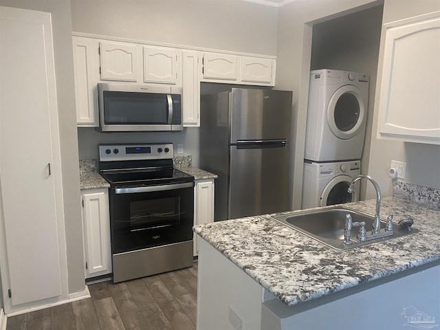 kitchen featuring stacked washer / drying machine, sink, light stone counters, appliances with stainless steel finishes, and white cabinets