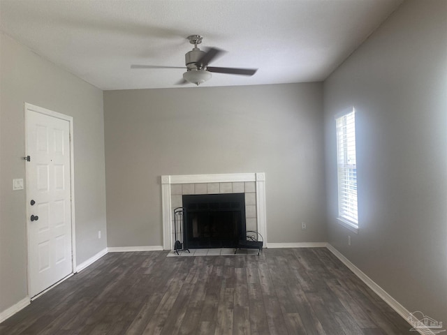 unfurnished living room with a tiled fireplace, dark wood-type flooring, and ceiling fan