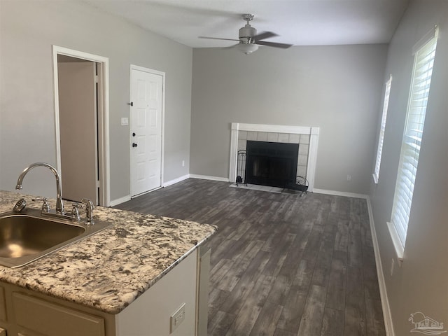 kitchen featuring a tile fireplace, sink, ceiling fan, light stone countertops, and dark wood-type flooring