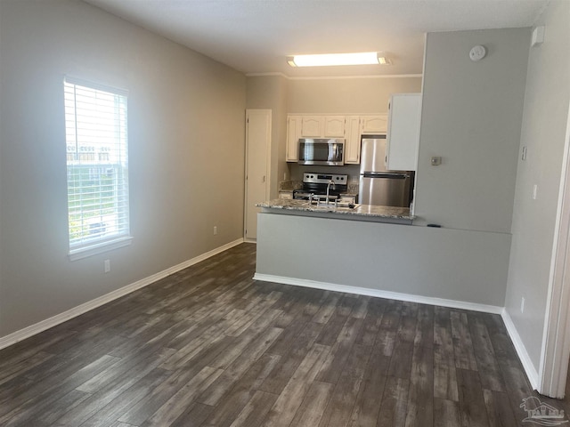 kitchen with appliances with stainless steel finishes, dark hardwood / wood-style flooring, kitchen peninsula, and white cabinets