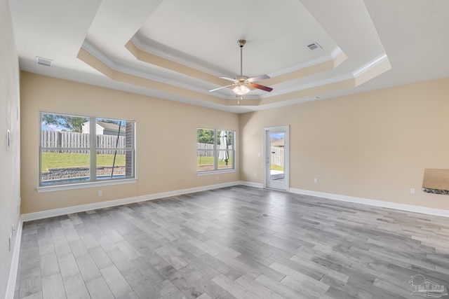 unfurnished room with light wood-type flooring, a tray ceiling, ceiling fan, and ornamental molding