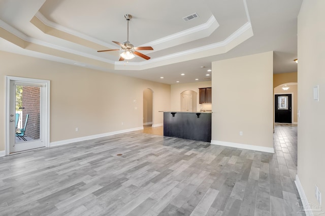 unfurnished living room with light wood-type flooring, a tray ceiling, ceiling fan, and crown molding