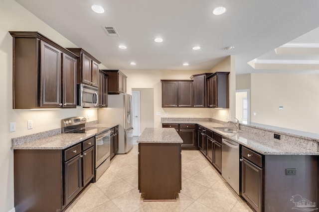 kitchen featuring sink, stainless steel appliances, light stone counters, kitchen peninsula, and a kitchen island