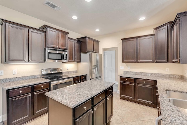 kitchen with dark brown cabinetry, light stone counters, light tile patterned floors, and stainless steel appliances