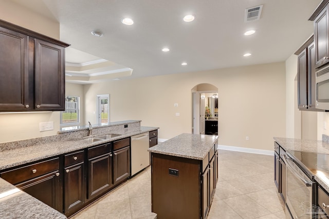 kitchen with light stone counters, stainless steel dishwasher, dark brown cabinets, sink, and a kitchen island