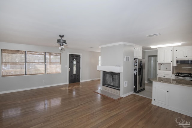 unfurnished living room featuring visible vents, dark wood-type flooring, baseboards, and a glass covered fireplace