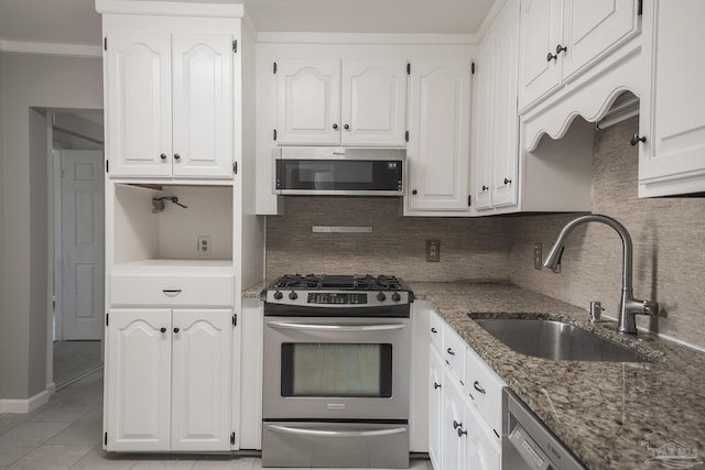 kitchen with a sink, stainless steel appliances, white cabinetry, and dark stone counters