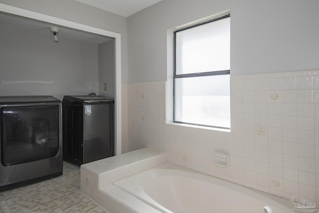 bathroom featuring a garden tub, tile walls, and washer and clothes dryer