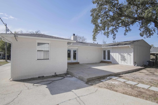 back of property with brick siding, central AC unit, french doors, a chimney, and a patio