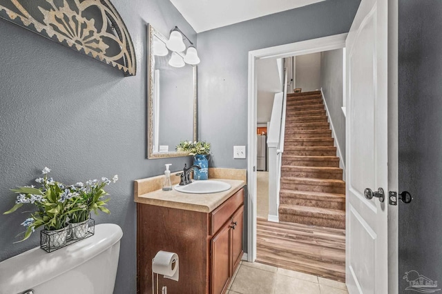 bathroom with a textured wall, vanity, toilet, tile patterned floors, and baseboards