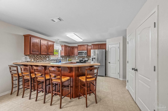 kitchen featuring appliances with stainless steel finishes, light countertops, a peninsula, backsplash, and visible vents