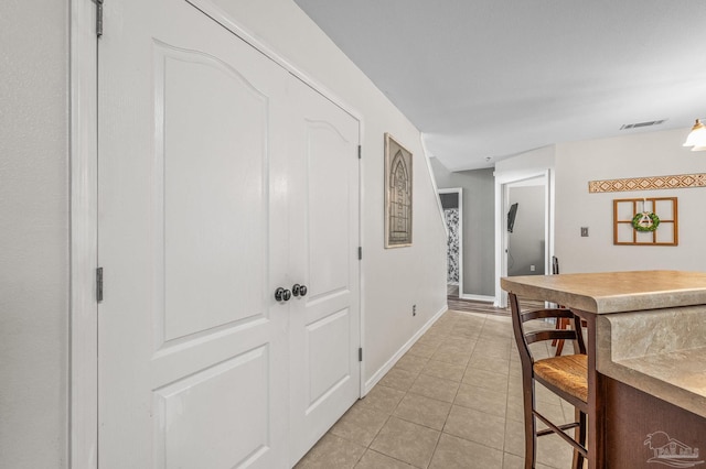hall featuring baseboards, visible vents, and light tile patterned floors