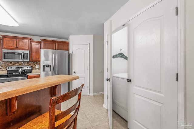 kitchen with appliances with stainless steel finishes, light countertops, washer / clothes dryer, a kitchen bar, and backsplash