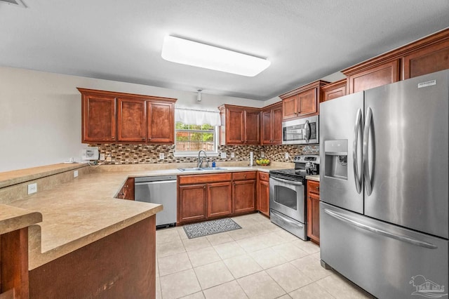 kitchen featuring appliances with stainless steel finishes, a sink, light countertops, a peninsula, and decorative backsplash