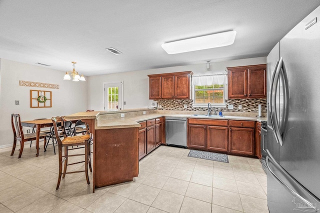 kitchen featuring a notable chandelier, a sink, stainless steel appliances, a peninsula, and tasteful backsplash