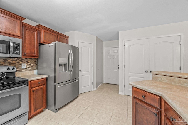 kitchen with baseboards, light countertops, tasteful backsplash, light tile patterned floors, and stainless steel appliances