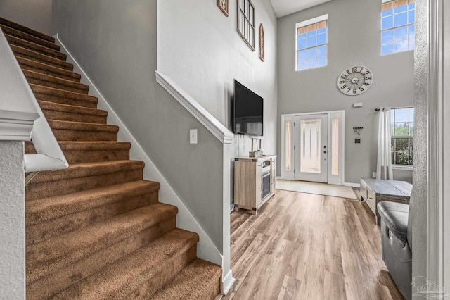 foyer entrance featuring stairs, a wealth of natural light, light wood finished floors, and a towering ceiling