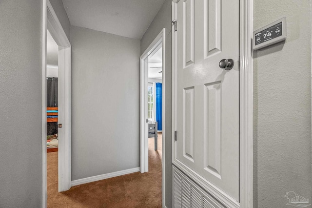 hallway featuring carpet flooring, baseboards, and a textured wall