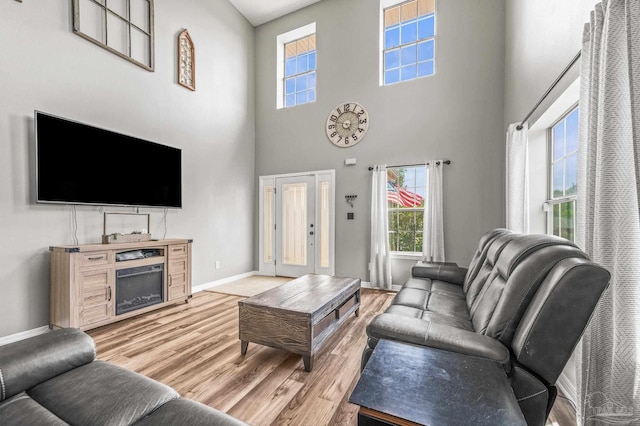 living room featuring baseboards, a fireplace, light wood finished floors, and a towering ceiling