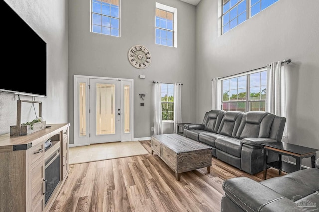 living area featuring baseboards, light wood-type flooring, and a towering ceiling