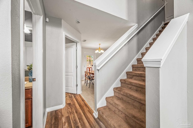 staircase featuring wood finished floors and a notable chandelier