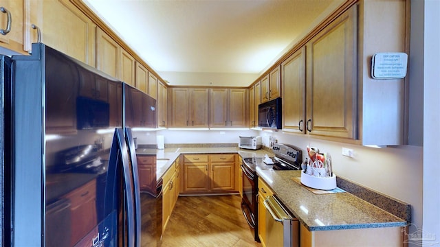 kitchen featuring light stone counters, black appliances, and light wood-type flooring