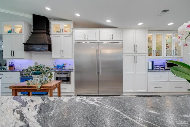 kitchen featuring crown molding, custom range hood, white cabinets, stainless steel appliances, and decorative backsplash