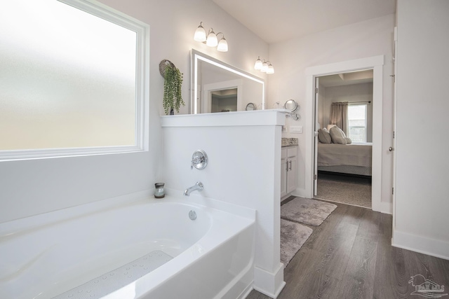 ensuite bathroom with ensuite bathroom, wood finished floors, vanity, baseboards, and a bath