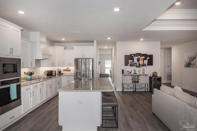 kitchen with appliances with stainless steel finishes, a center island with sink, and white cabinetry