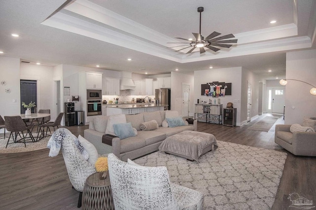 living area with ceiling fan, recessed lighting, dark wood-style floors, a tray ceiling, and crown molding