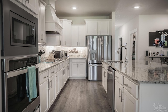 kitchen with stainless steel appliances, white cabinetry, custom range hood, and a sink