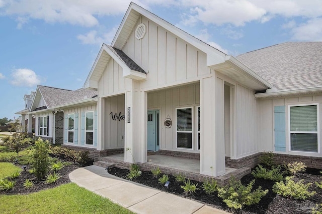 entrance to property featuring covered porch, roof with shingles, brick siding, and board and batten siding