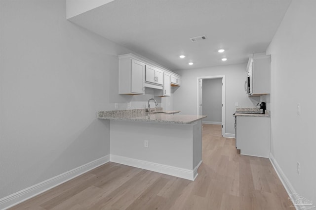 kitchen with a peninsula, light stone countertops, baseboards, and white cabinetry