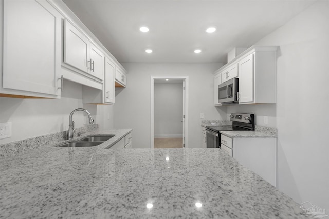 kitchen with stainless steel appliances, white cabinets, a sink, and light stone countertops