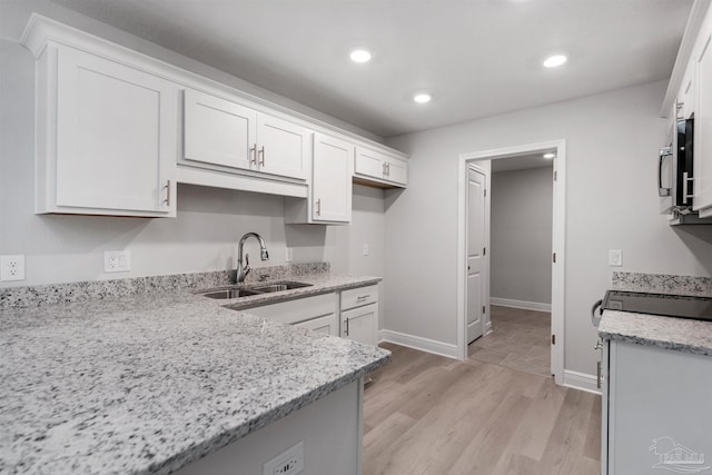 kitchen featuring light stone counters, light wood-type flooring, a sink, and white cabinets