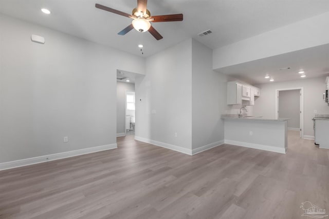 unfurnished living room with a sink, a ceiling fan, baseboards, visible vents, and light wood-style floors