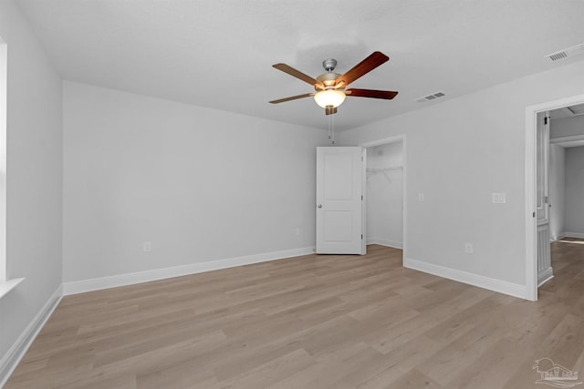 unfurnished bedroom with a spacious closet, light wood-type flooring, visible vents, and baseboards