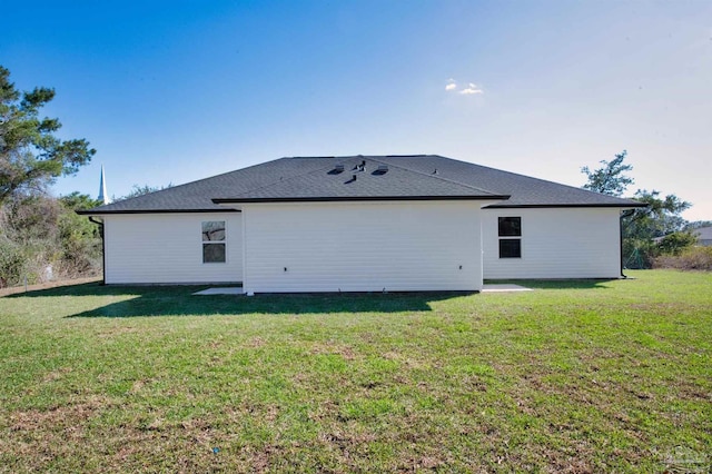 rear view of house with a shingled roof and a lawn