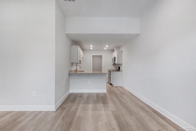 unfurnished living room with light wood-type flooring, a sink, baseboards, and recessed lighting