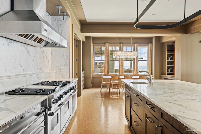 kitchen featuring sink, double oven range, pendant lighting, light stone countertops, and wall chimney range hood