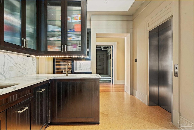 bar featuring light stone counters, backsplash, dark brown cabinets, and elevator