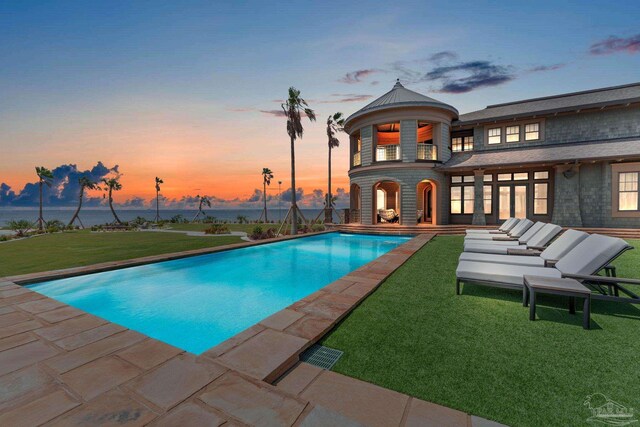 pool at dusk with a yard and a patio area