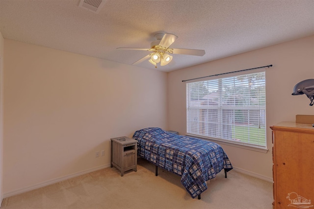 bedroom featuring ceiling fan, light colored carpet, and a textured ceiling