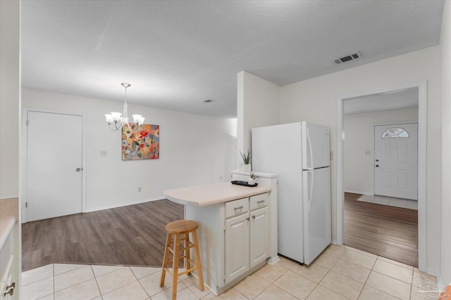 kitchen with a breakfast bar, an inviting chandelier, decorative light fixtures, light tile patterned floors, and white fridge