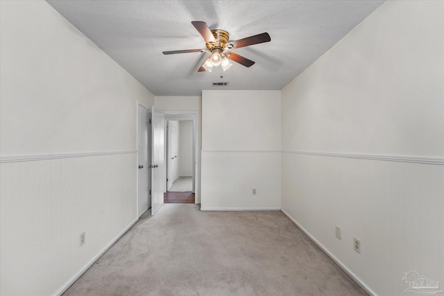 spare room featuring ceiling fan, light colored carpet, and a textured ceiling