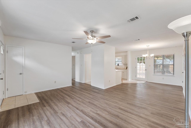 unfurnished living room with ceiling fan with notable chandelier and wood-type flooring