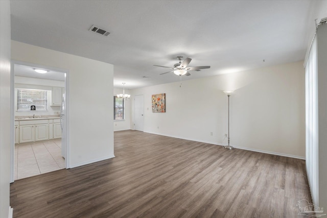 unfurnished living room with sink, ceiling fan with notable chandelier, and light hardwood / wood-style floors