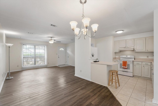 kitchen with hanging light fixtures, electric range, a kitchen breakfast bar, light hardwood / wood-style floors, and ceiling fan with notable chandelier