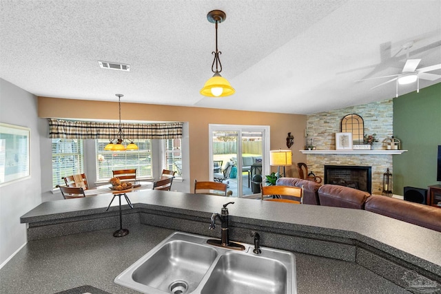 917 Broken Arrow Ln, Pensacola, FL 32533 - kitchen featuring a sink, vaulted ceiling, dark countertops, a stone fireplace, and a textured ceiling